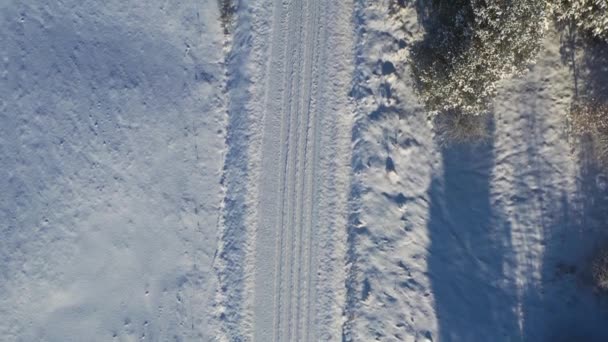 Luftaufnahme von oben nach unten, die im Winter entlang der weißen, schneebedeckten Schotterstraße fliegt - Filmmaterial, Video