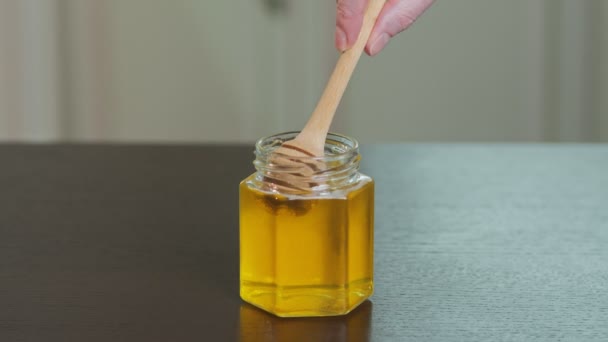 Nestemäinen orgaaninen raaka hunaja lasipurkissa, jossa on puinen hunajavaippa. - Materiaali, video