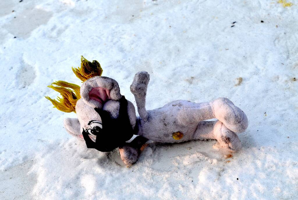 Vemos un juguete para niños que lleva una máscara protectora.El juguete, aparentemente perdido, yace en la nieve.. - Foto, Imagen