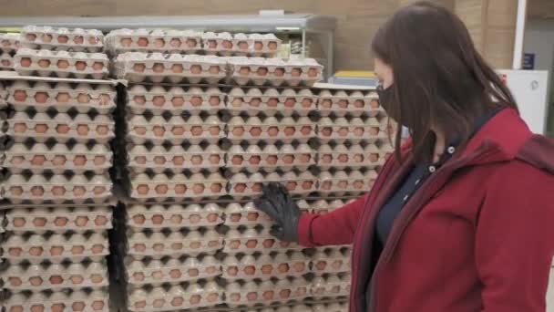 Nainen yllään naamio ja käsineet virusta vastaan valitse kananmunat ruokakaupassa - Materiaali, video