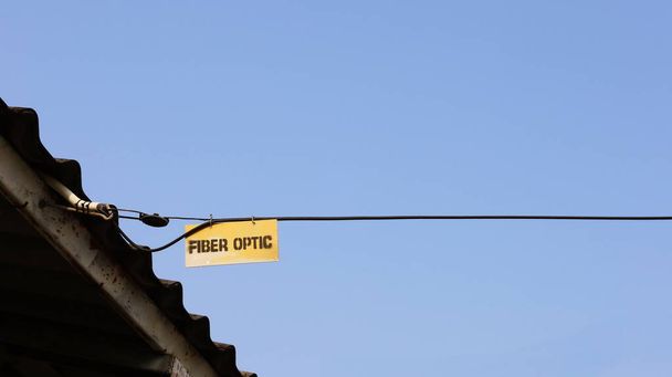 Závěsné značky na optických kabelech. Štítek "FIBER OPTIC" označuje typ černého kabelu na pozadí, střeše a modré obloze s kopírovacím prostorem. Vyberte předmět a soustřeďte se. - Fotografie, Obrázek
