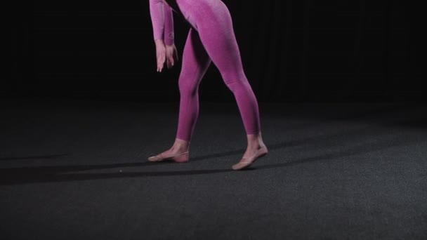 Giovane ginnasta femminile cammina nello studio nero e si siede su una spaccatura - Filmati, video