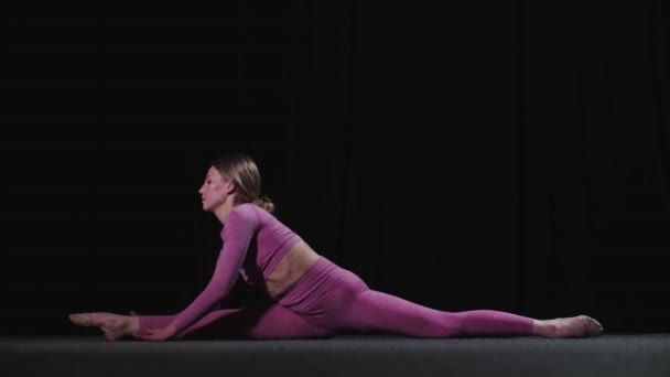 Giovane ginnasta femminile si siede su spaccature e sporgendosi in avanti per le dita dei piedi - Filmati, video