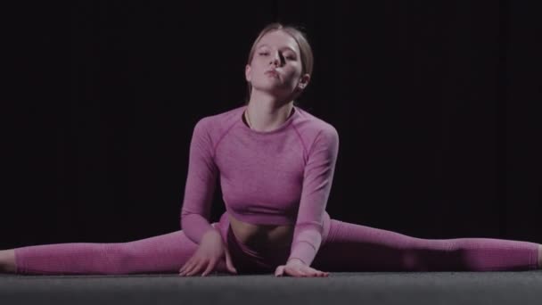 Mladá gymnastka sedí na štěrbinách a naklání se dopředu - Záběry, video