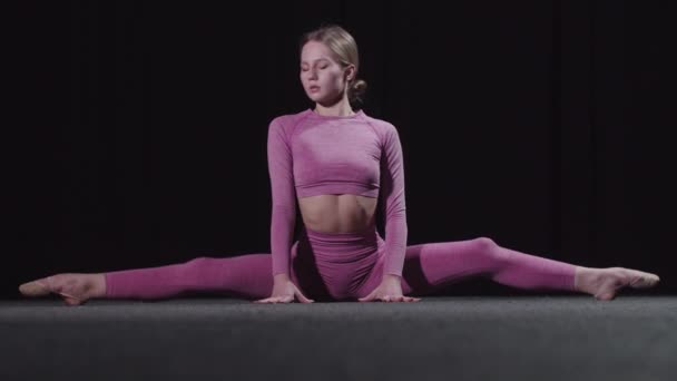 Jonge vrouwelijke turnster in roze kleren zit op splitten en leunend naar voren voor haar tenen - Video