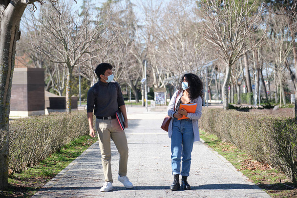 Zwei lateinamerikanische Studenten, die in sozialem Abstand gehen und Gesichtsmasken tragen, schauen einander an. Neue Normalität auf dem Universitätscampus. - Foto, Bild