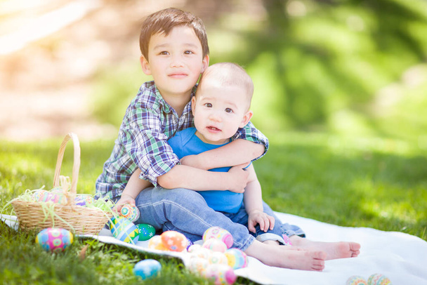 Sekarotuinen kiinalainen ja valkoihoinen pojat ulkona puistossa leikkii pääsiäismunia. - Valokuva, kuva