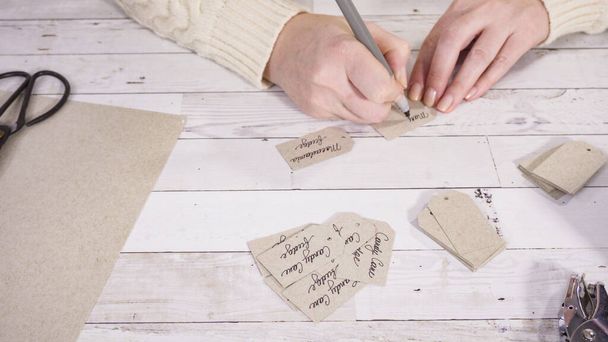 Step by step. Labeling brown paper gift tags with a black marker. - Photo, Image