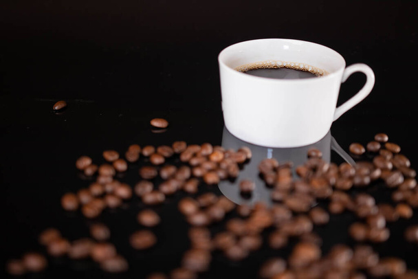 Geroosterde koffiebonen en witte mok op zwarte achtergrond - Foto, afbeelding