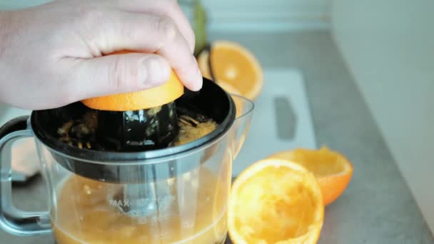 Vista de la mano del hombre mientras se exprime la fruta fresca de naranja en el exprimidor, preparación del desayuno saludable, jugo de vitaminas - Imágenes, Vídeo