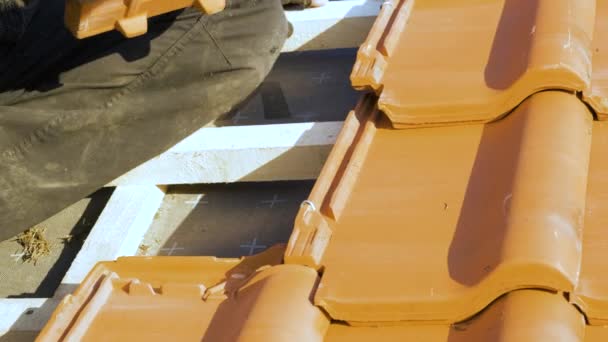 Großaufnahme von Arbeiterhänden, die gelbe Keramik-Dachziegel auf Holzplatten montieren, die das Dach eines Wohnhauses bedecken, das im Bau ist. - Filmmaterial, Video