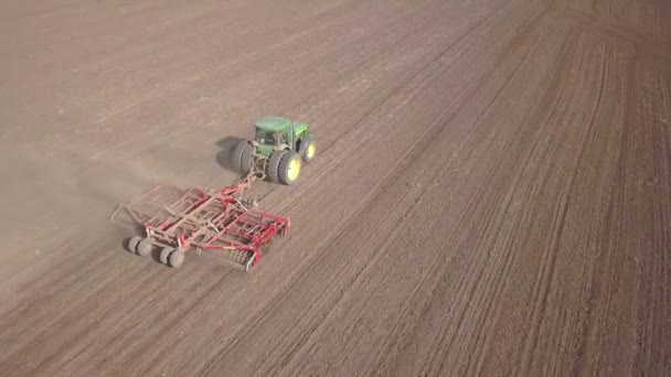 Luftaufnahme von oben nach unten von grünem Traktor, der Boden anbaut und ein trockenes Feld aussät. Landwirt bereitet Land mit Pflanzbeet-Grubber als Teil der Vorsaat-Aktivitäten im zeitigen Frühjahr vor. - Filmmaterial, Video