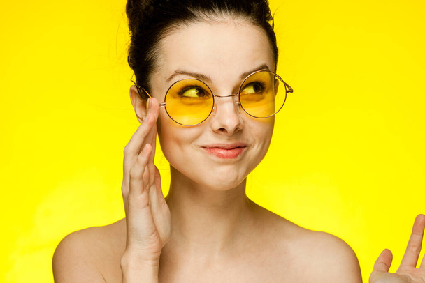 cheerful woman naked shoulders yellow glasses gathered hair Studio - Foto, Imagen
