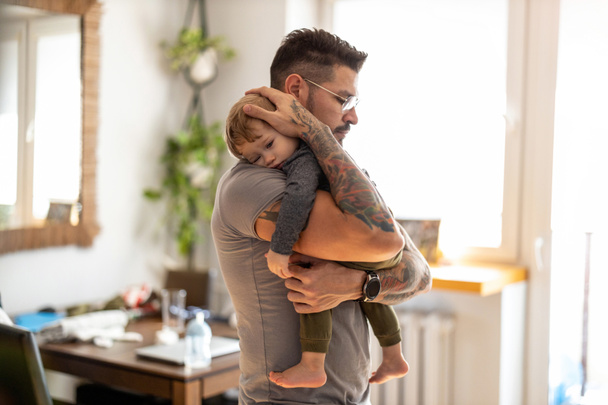 Papá poniendo a dormir al niño en sus brazos en casa - Foto, Imagen