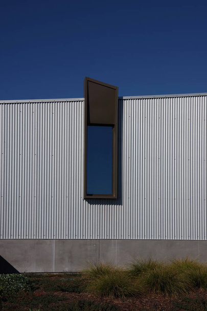 Vista parcial de un edificio industrial con una única ventana que refleja el cielo azul - Foto, imagen