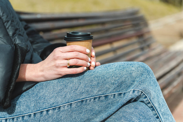 handen van onherkenbare blanke vrouw met een kop koffie in een park - Foto, afbeelding