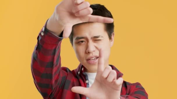 Ασιάτης τύπος συλλαμβάνει Στιγμιαία Framing Πρόσωπο με τα δάχτυλα, κίτρινο φόντο - Πλάνα, βίντεο