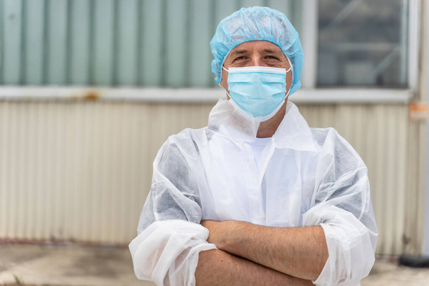 Porträt eines kaukasischen Mannes mit Schutzmaske und Bouffant-Mütze - Junger männlicher Arzt oder Wissenschaftler bei der Arbeit vor dem Laborkrankenhaus im Kopierraum - Foto, Bild