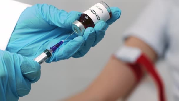 Covid-19 vaccinatie. Close-up van de hand van de arts die het vaccin in de spuit neemt, patiënt die op de achtergrond wacht, slow motion - Video