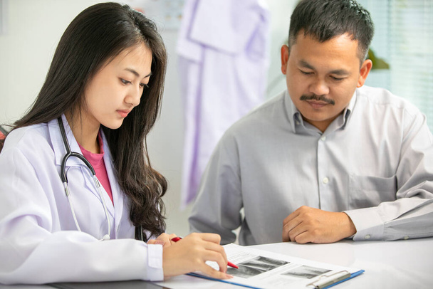 Ázsiai nők Orvos és férfi páciens beszélgetés az eredményekről röntgen képek a klinika irodájában - Fotó, kép