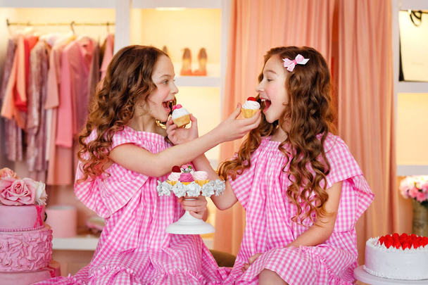 Due ragazze adolescenti in abiti rosa e lunghi capelli arricciati a una festa di torta. Provano le torte. - Foto, immagini