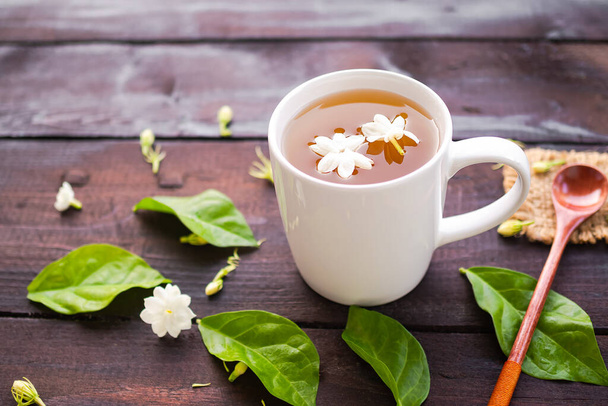 Жасмин чай з квітами жасмину в білій чашці з дерев'яною ложкою на чорному дереві. гарячий чай з природи для здоров'я. випити таїланду і випити вранці. концепція трав'яного напою
. - Фото, зображення