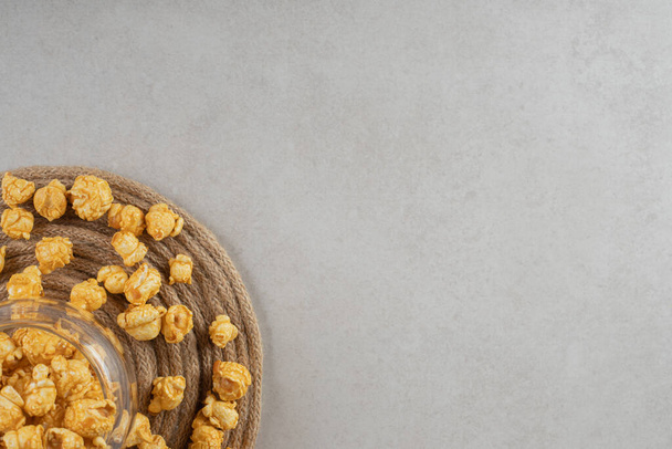 Full glass bowl ringed with caramel coated popcorn on a trivet on marble background. High quality photo - Photo, Image