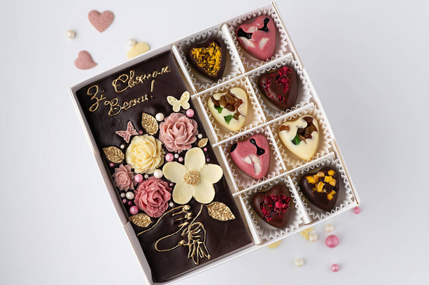 un conjunto de chocolates hechos a mano en forma de corazones y azulejos de ingredientes naturales con la inscripción en ucraniano: Feliz primavera - Foto, imagen