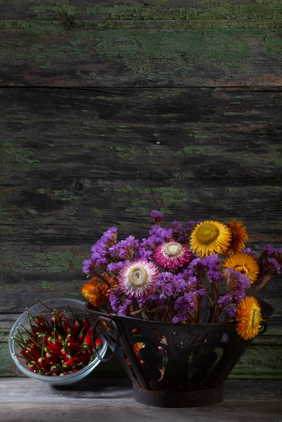 Stillleben Nahaufnahme Foto von Strauß lebhafter getrockneter Blumen und Paprika auf hölzernem Hintergrund - Foto, Bild