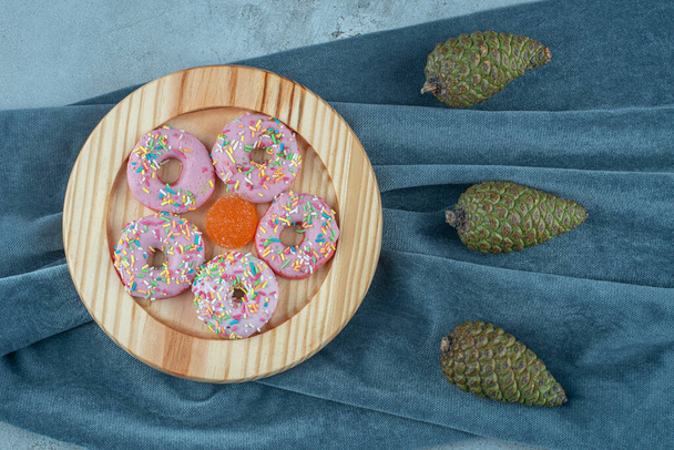 Piece of fabric under pine cones and a platter of donuts on textile background. High quality photo - Photo, Image