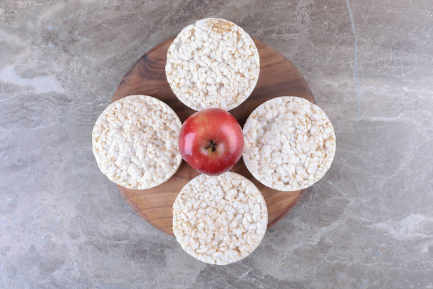 Jabłko i dmuchane ciastka ryżowe na drewnianej tacy, na marmurowym tle. Wysokiej jakości zdjęcie - Zdjęcie, obraz
