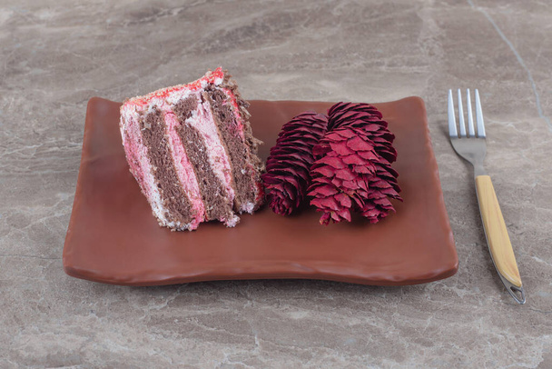 Шматочок торта і червоні соснові шишки на тарілці поруч з виделкою на мармуровому фоні. Високоякісна фотографія
 - Фото, зображення