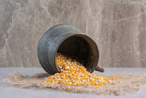 Jarra de metal vertiendo granos de maíz sobre un trozo de tela sobre fondo de mármol. Foto de alta calidad - Foto, imagen