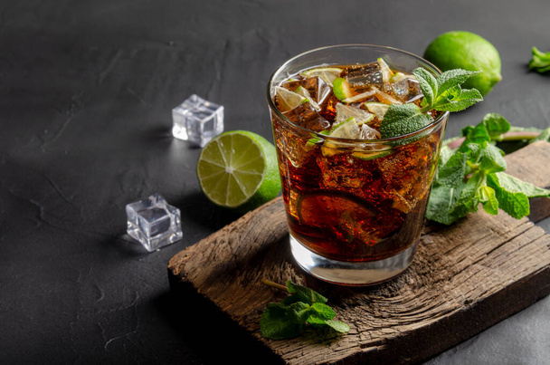 cuba libre, rum and cola cocktail in glass with a lime and mint on black - Photo, Image