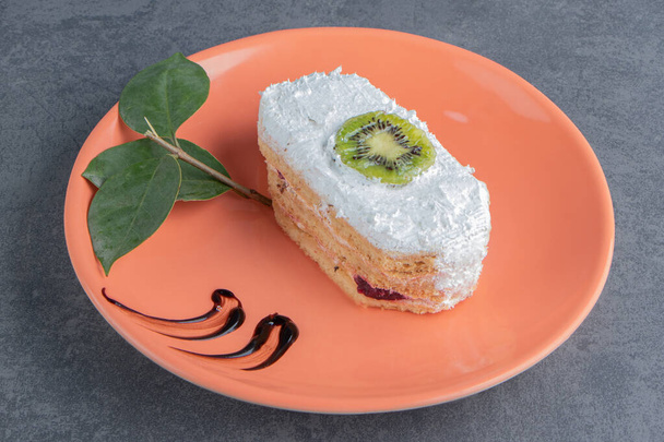 Un pedazo de pastel cremoso con rebanada de kiwi y hojas. Foto de alta calidad - Foto, Imagen