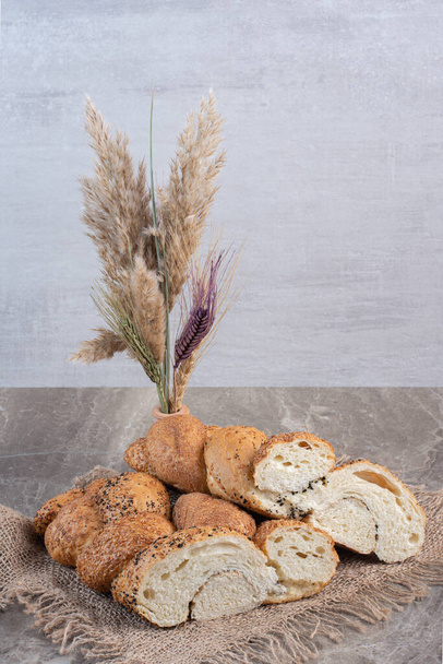 Vase de tiges de blé décoratives à côté d'un paquet de pains de pain tranchés enduits de sésame sur fond de marbre. Photo de haute qualité - Photo, image