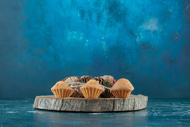 Cupcakes y una corona de pino dispuestos en una tabla de madera sobre fondo azul. Foto de alta calidad - Foto, imagen