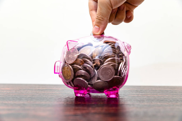 Mão de homem colocando moeda em banco porquinho cheio de moedas, economizando conceito de dinheiro - Foto, Imagem