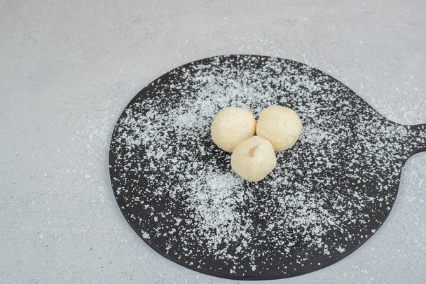 Uma tábua de corte escura com massa redonda com açúcar em pó. Foto de alta qualidade - Foto, Imagem