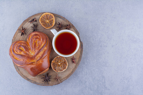 Anis, tranche de citron séchée, une tasse de thé et un petit pain sucré sur une planche de bois sur fond de marbre. Photo de haute qualité - Photo, image