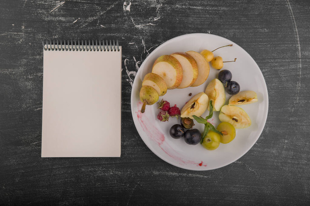 vista superior de frutas e bagas em fatias frescas no prato e notebook em branco - Foto, Imagem