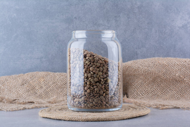 Jar full of brown lentil sitting on a trivet on marble background. High quality photo - Photo, Image