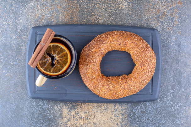 Tasse en métal de thé avec tranche de citron séchée, bâton de cannelle et un bagel sur une planche sur fond de marbre. Photo de haute qualité - Photo, image