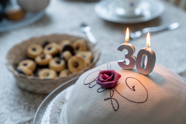 Narozeninový oslavný dort s hořícími svíčkami ve formě čísel a prostřený narozeninový stůl. Narozeninová oslava ve třiceti letech. - Fotografie, Obrázek