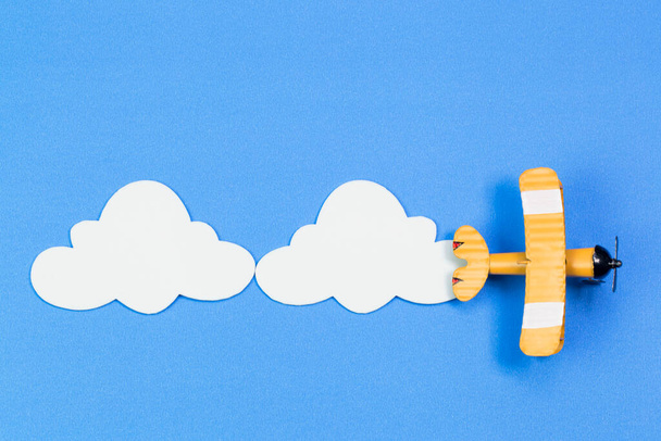 Παιδικό αεροπλάνο σε φόντο μπλε ουρανού με χάρτινα σύννεφα. Η έννοια ταξίδια και αεροπορικές εταιρείες - Φωτογραφία, εικόνα