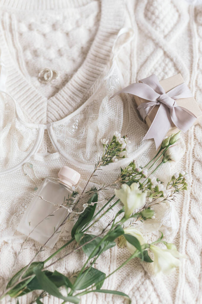 Stylowa bielizna koronkowa, butelka perfum, nowoczesna biżuteria i pudełko na przytulny beżowy sweter z wiosennymi kwiatami. Miękki, modny kobiecy wizerunek. Szczęśliwego Dnia Kobiet. Niezbędne dla kobiet, zapach - Zdjęcie, obraz