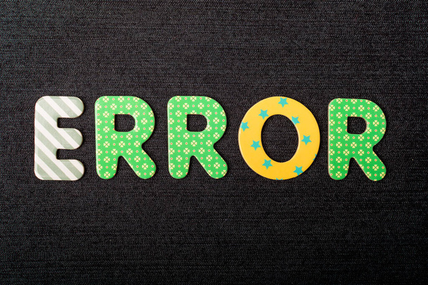 Κάρτα με τη λέξη λάθους από μικτά ζωηρά χρωματιστά ξύλινα γράμματα σε ένα υφασμένο σκούρο μαύρο ύφασμα υλικό που μπορεί να χρησιμοποιηθεί ως μήνυμα - Φωτογραφία, εικόνα