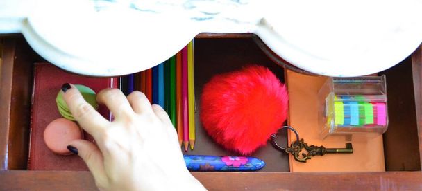 Im Inneren einer offenen Schublade befinden sich Buntstifte, ein Buch, ein roter Schlüsselanhänger mit Schlüssel, ein mehrfarbiger Stift und farbiges Klebeband - Foto, Bild