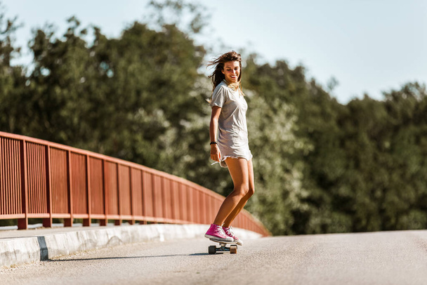 Νεαρή σπορ γυναίκα ιππασία στο skateboard στο δρόμο. - Φωτογραφία, εικόνα