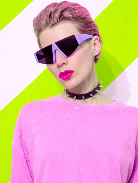 Acid Party Model s krátkými vlasy nosí stylové doplňky agresivní špunt a futuristické sluneční brýle. Trendy každodenní pouliční oblečení v detailech - Fotografie, Obrázek